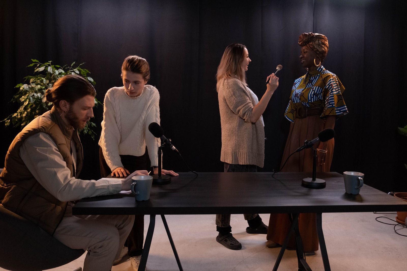Four co-hosts gathered around a table with microphones, recording a round-table conversation